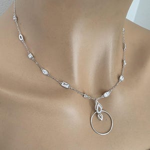 May include: A silver-toned necklace featuring a delicate chain interspersed with various small, clear, faceted stones in round, pear, and rectangular shapes. The necklace includes a central pendant consisting of a teardrop-shaped element above a plain ring.
