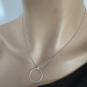 May include: A silver-toned necklace featuring a delicate ball chain and a circular pendant. The pendant has a textured, ridged surface and is suspended from a small, simple silver loop attached directly to the chain, creating a clean look.