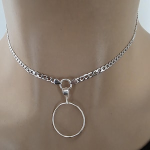 May include: A silver-toned necklace featuring a delicate curb chain and a central circular pendant. The pendant is suspended from a small jump ring attached to the chain, creating a simple, clean design that rests against the neck.