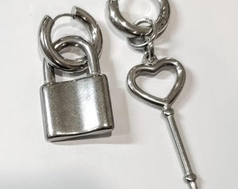 Op de afbeelding: Een paar zilveren oorbellen, een met een hangslotbedel en de andere met een hartvormige sleutelbedel.