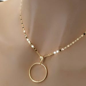 May include: A gold necklace featuring a delicate chain with flat, reflective links and a simple, circular pendant suspended from a small, tapered bail. The metal has a polished, warm yellow tone that catches the light, creating a bright, metallic sheen.