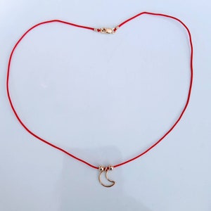 May include: A red string necklace with a gold crescent moon charm.