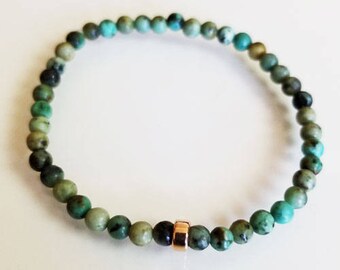 May include: A turquoise gemstone bracelet with a gold accent bead. The bracelet is made of small, round beads and is approximately 7 inches in length.