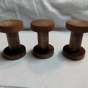 May include: Three wooden display stands with a dark brown finish. Each stand has a circular base, a cylindrical stem, and a circular top. The stands are arranged on a white surface.