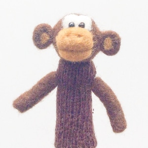 Peut inclure: Une marionnette de doigt en feutre marron en forme de singe. Le singe a un visage marron avec un nez brun clair et des yeux blancs. Le singe porte un pull marron.