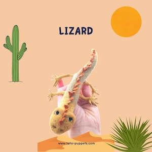 May include: A felt hand puppet of a lizard with orange and brown accents. The puppet is held in a hand against a light orange background with a cartoon cactus and a yellow sun.