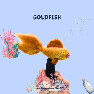 May include: A felt finger puppet of a goldfish with orange and yellow fur, swimming with bubbles coming out of its mouth. The puppet is on a hand with coral and seaweed in the background. The text "GOLDFISH" is at the top of the image.