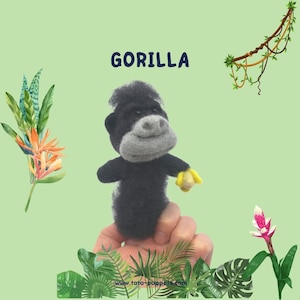 May include: A handmade black and gray gorilla finger puppet with a yellow banana. The word "GORILLA" is written in blue above the puppet. The background is light green with tropical plants and vines.