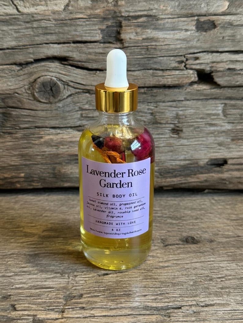 Puede incluir: Una botella de vidrio transparente de aceite corporal de seda Lavender Rose Garden con tapa dorada y cuentagotas blanco. La botella contiene flores secas y aceite. La etiqueta dice "Lavender Rose Garden". La botella es de 118 ml.