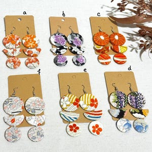 May include: Six pairs of earrings with three tiers of fabric circles. The fabric is patterned with flowers, geometric shapes, and abstract designs. The earrings are in various colors, including purple, orange, red, blue, and white.