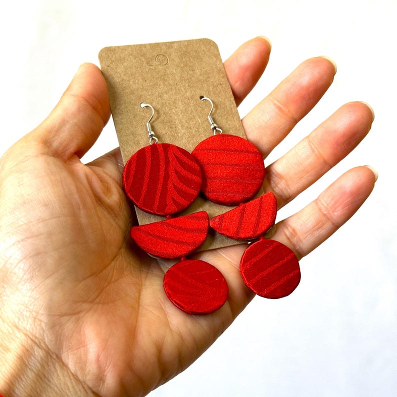 May include: Red fabric earrings with a geometric design. The earrings are made of three circles and two half-circles.
