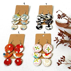 May include: Four pairs of earrings with different patterns. Each pair has three pieces, a large circle, a half-circle, and a smaller circle. The patterns include floral, geometric, and abstract designs. The earrings are displayed on brown card stock with the letters 'q', 'r', 't', and 's' written on them.