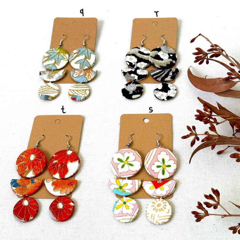 May include: Four pairs of earrings with different patterns. Each pair has three pieces, a large circle, a half-circle, and a smaller circle. The patterns include floral, geometric, and abstract designs. The earrings are displayed on brown card stock with the letters 'q', 'r', 't', and 's' written on them.