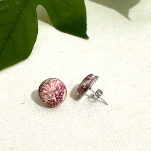 May include: A pair of silver stud earrings with a white and pink patterned design.