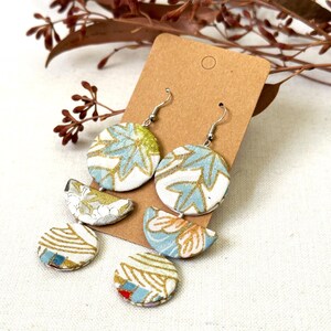 May include: A pair of dangle earrings with a blue and gold floral pattern. The earrings are made of fabric and have a silver hook.