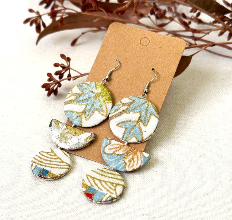 May include: A pair of dangle earrings with a blue and gold floral pattern. The earrings are made of fabric and have a silver hook.
