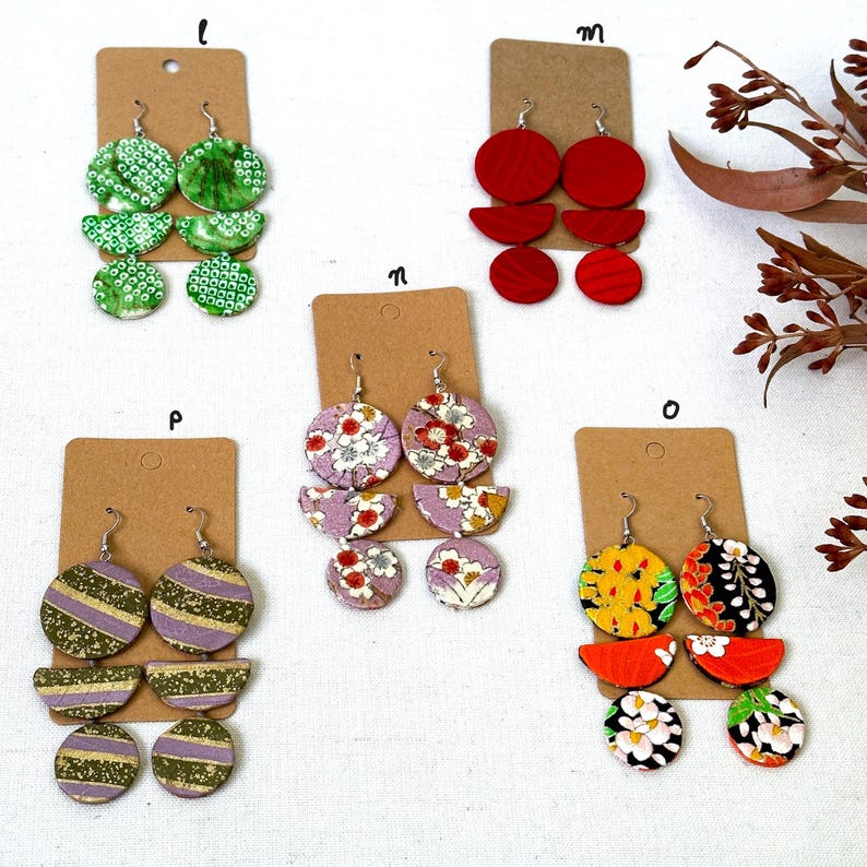 May include: Five pairs of earrings with different patterns and colors. The earrings are made of wood and have a geometric design. The earrings are displayed on a white background.