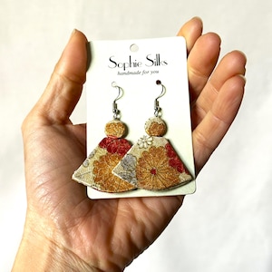 May include: A pair of drop earrings on a white display card labelled Sophie Silks handmade for you. The earrings feature a small circular top and a larger fan-shaped bottom, both decorated with a metallic gold, red, and silver floral pattern.