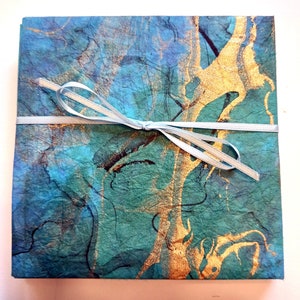 May include: A stack of blue and green paper with gold accents, tied with a light blue ribbon. The paper has a textured, marbled look.
