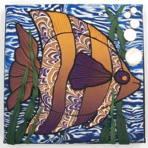 May include: A colorful, hand-painted ceramic tile featuring a stylized fish with orange, brown, purple, and white patterns. The fish is surrounded by green seaweed and white bubbles.