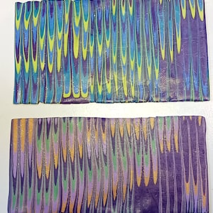 May include: Two rows of colorful polymer clay canes with a marbled pattern. The top row has a blue, green, and purple pattern. The bottom row has a purple, green, and orange pattern.