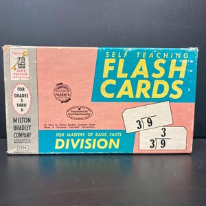 May include: Vintage Milton Bradley "Self Teaching Flash Cards" box for division, grades 3-6. The box is pink and blue with the words "FLASH CARDS" in large yellow letters. Includes sample math problems.