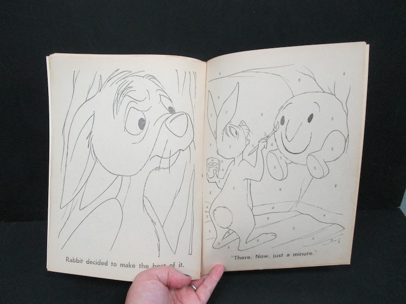 May include: A black and white illustration of a rabbit painting a round, smiling character. The text "There. Now, just a minute." is below the illustration. The illustration is from a children's book.