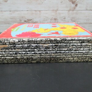 May include: A stack of ten vintage children's books with silver covers and black illustrations. The top book has a red, yellow, and blue cover with the text "The Red Book" and an illustration of Big Bird.