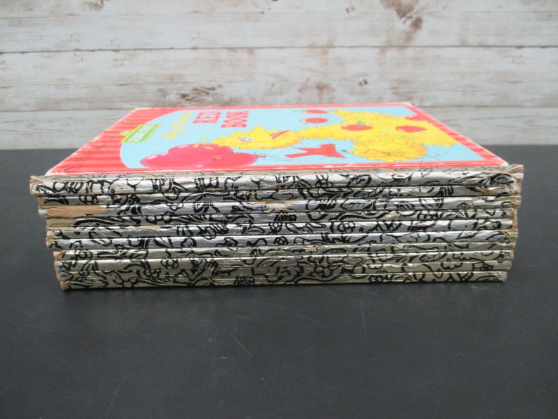 May include: A stack of ten vintage children's books with silver covers and black illustrations. The top book has a red, yellow, and blue cover with the text "The Red Book" and an illustration of Big Bird.