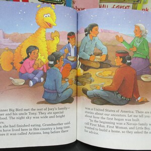 May include: A children's book illustration depicting a yellow Big Bird character with a group of people sitting around a campfire. The text reads, "At dinner Big Bird met the rest of Joey's family - his mother and his uncle Tony. They ate special Navajo food. The night sky was wide and bright with stars. When she had finished eating, Grandmother said, "Navajos have lived here in this country a long time, long before it was called Arizona, long before there was a United States of America. There are many stories about our ancestors. Let me tell you one about how the first hogan was built. "In the beginning was a Navajo family whom we call First Man, First Woman, and Little Boy. They wanted to build a home, so they asked the animals for advice."