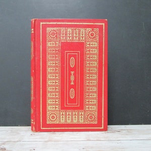 May include: A red hardcover book with a gold decorative design on the cover. The design features a repeating pattern of crosses and circles.