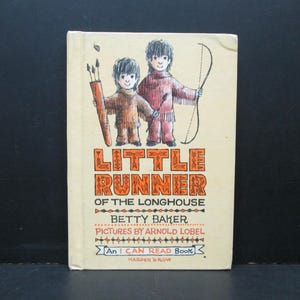 May include: A book cover with an illustration of two children in Native American clothing holding bows and arrows. The title of the book is "Little Runner of the Longhouse" by Betty Baker with illustrations by Arnold Lobel. It is an I Can Read Book published by Harper Row.
