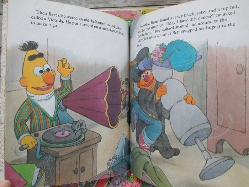 May include: Bert, a yellow Sesame Street character, plays a record on a vintage record player with a large, purple horn. Ernie, another Sesame Street character, dances with a snowman wearing a blue hat and a black jacket.