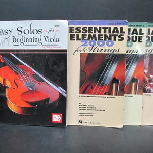 May include: Four music books for viola and cello. The books are titled "Easy Solos for Beginning Viola", "Essential Elements 2000 for Strings", "Essential Technique" and "Essential Technique". The books feature images of violas.