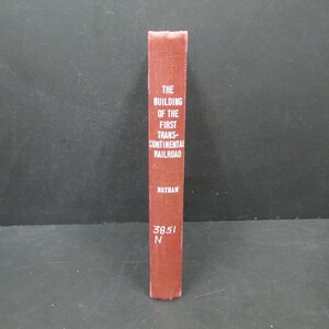 May include: A vintage book titled "The Building of the First Trans-Continental Railroad" by Nathan. The book has a textured, reddish-brown cover with white lettering. The spine also displays the numbers "3851" and the letter "N".