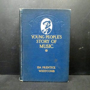 May include: A vintage blue book titled "Young People's Story of Music" by Ida Prentice Whitcomb. The cover features an embossed illustration of a person in a hat and a decorative border. The book is in good condition.