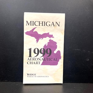 May include: A vintage 1999 Michigan Aeronautical Chart. The cover features the state's outline in purple, with the word "Michigan" above and "1999 AERONAUTICAL CHART" below. The MDOT Bureau of Aeronautics logo is at the bottom.
