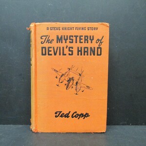 May include: An orange book cover with black text that reads "A Steve Knight Flying Story The Mystery of Devil's Hand" and "Ted Copp". The cover features a black and white illustration of a plane.