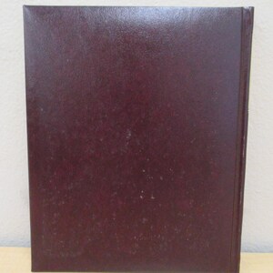 Puede incluir: Un libro de tapa dura de color burdeos oscuro con una cubierta lisa y texturizada.