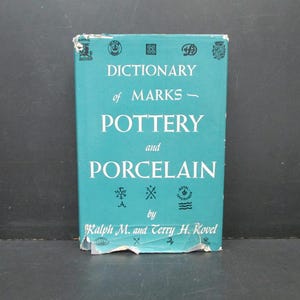 May include: A teal blue book titled "Dictionary of Marks - Pottery and Porcelain" by Ralph M. and Terry H. Kovel. The cover features several small black and white illustrations of pottery marks.