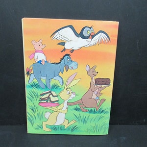 May include: A colourful illustration featuring Winnie the Pooh characters: Piglet riding on Eeyore, Rabbit carrying a stack of sandwiches, Kanga holding a cake, and Owl flying overhead. The background is a sunset orange with green grass.