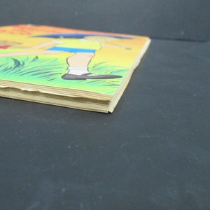 May include: A vintage children's book with a yellow, orange and green cover. The cover features an illustration of two children walking in a grassy field. The book is slightly worn and has a few creases.