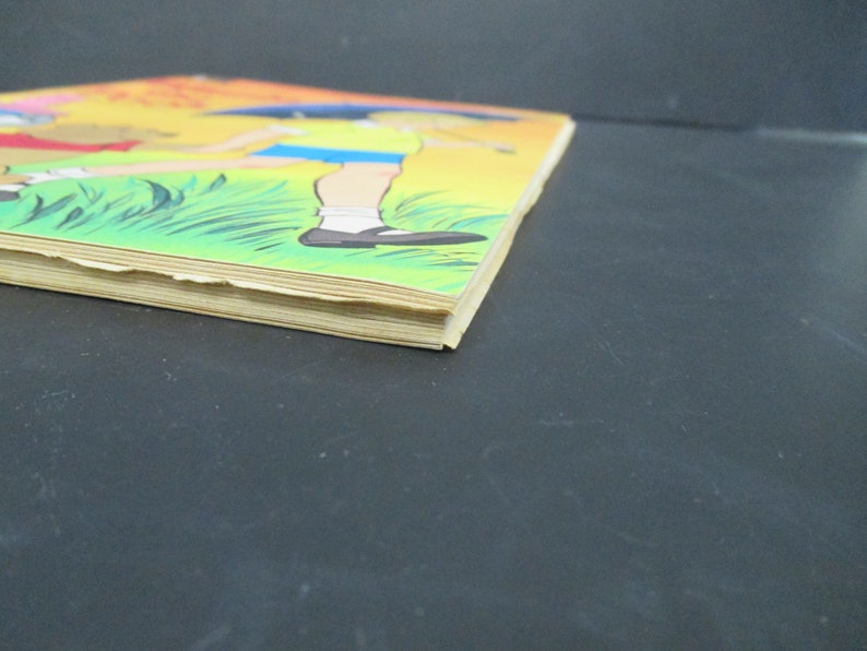 May include: A vintage children's book with a yellow, orange and green cover. The cover features an illustration of two children walking in a grassy field. The book is slightly worn and has a few creases.