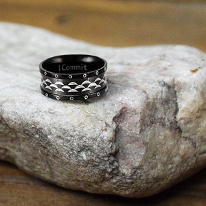 May include: A black and silver patterned ring with the inscription "I Commit" on the band.