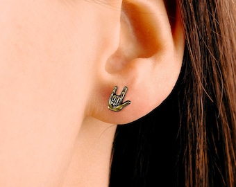 May include: A pair of gold-toned earrings featuring a small hand sign in the shape of the American Sign Language symbol for "I love you".