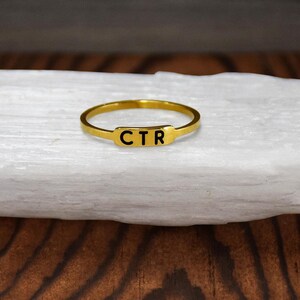 May include: A gold ring with the letters "CTR" engraved on a rectangular band.