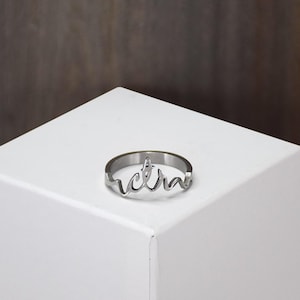 May include: A silver ring with the word "extra" written in a cursive font.