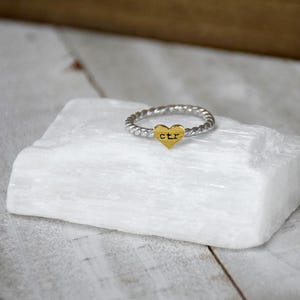 May include: A silver twisted band ring with a gold heart charm that says "CTR" on it.