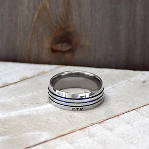May include: A silver ring with three blue lines around the band. The ring is engraved with the letters "CTR".