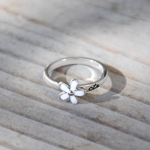 May include: A silver ring with a white flower charm and the word "cute" inscribed on the band.